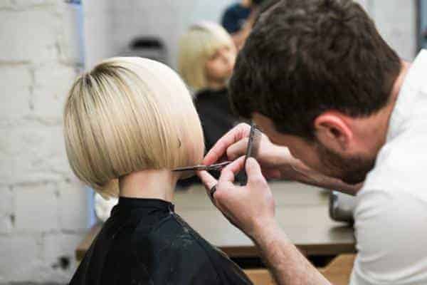 La coupe méthode globale. Coiffeur coupant les cheveux d'une cliente blonde dans un salon de coiffure avec des ciseaux en gros plan.